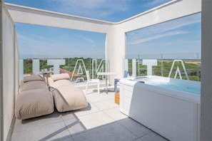 A balcony with a hot tub, lounge chairs, and a clear view of the landscape.
