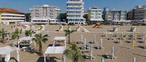 Une plage bordée de rangées de transats et de parasols, une aire de jeux pour enfants et, au loin, plusieurs immeubles à étages.