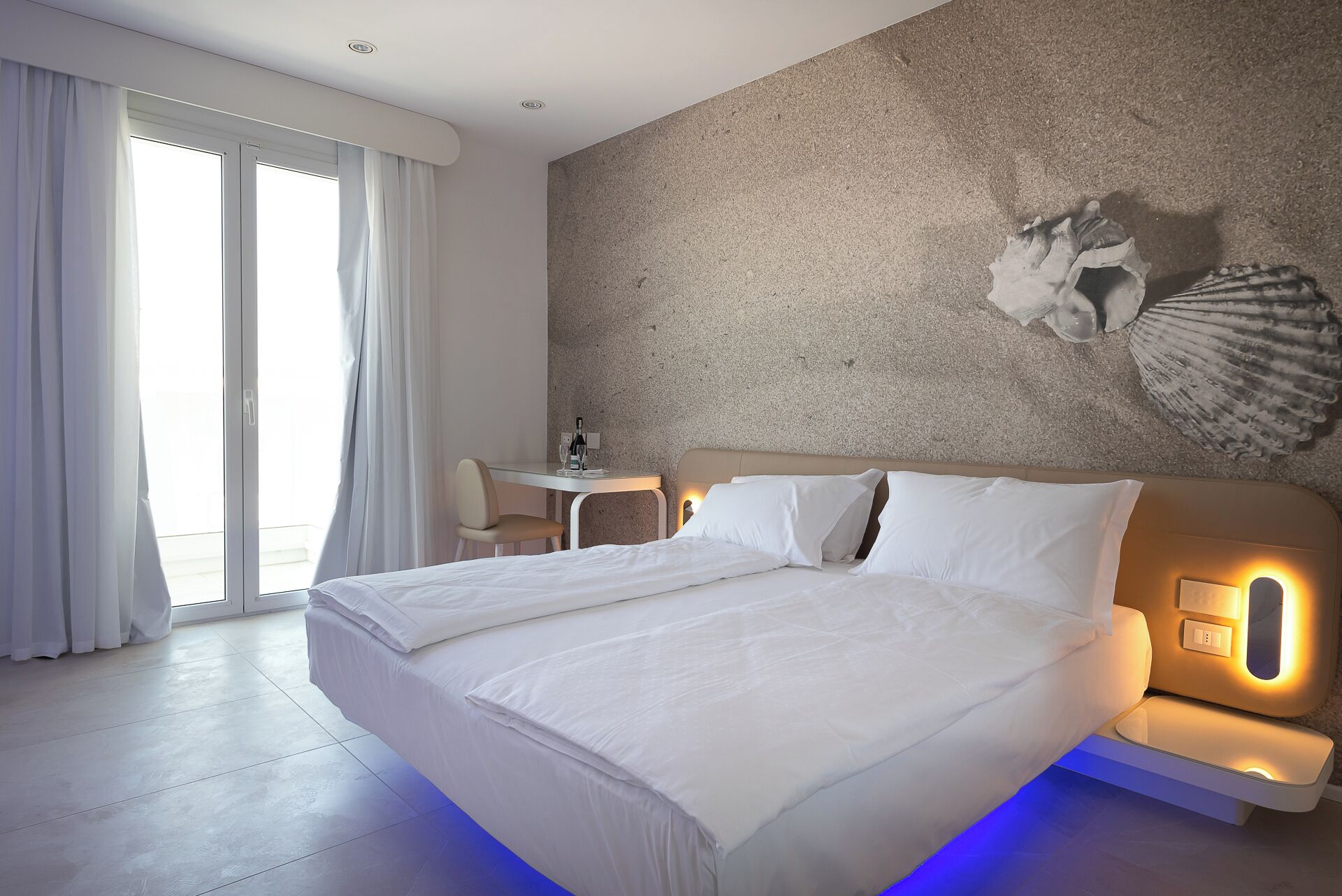 A modern hotel room with a large bed, a desk, and a view of the outdoors.