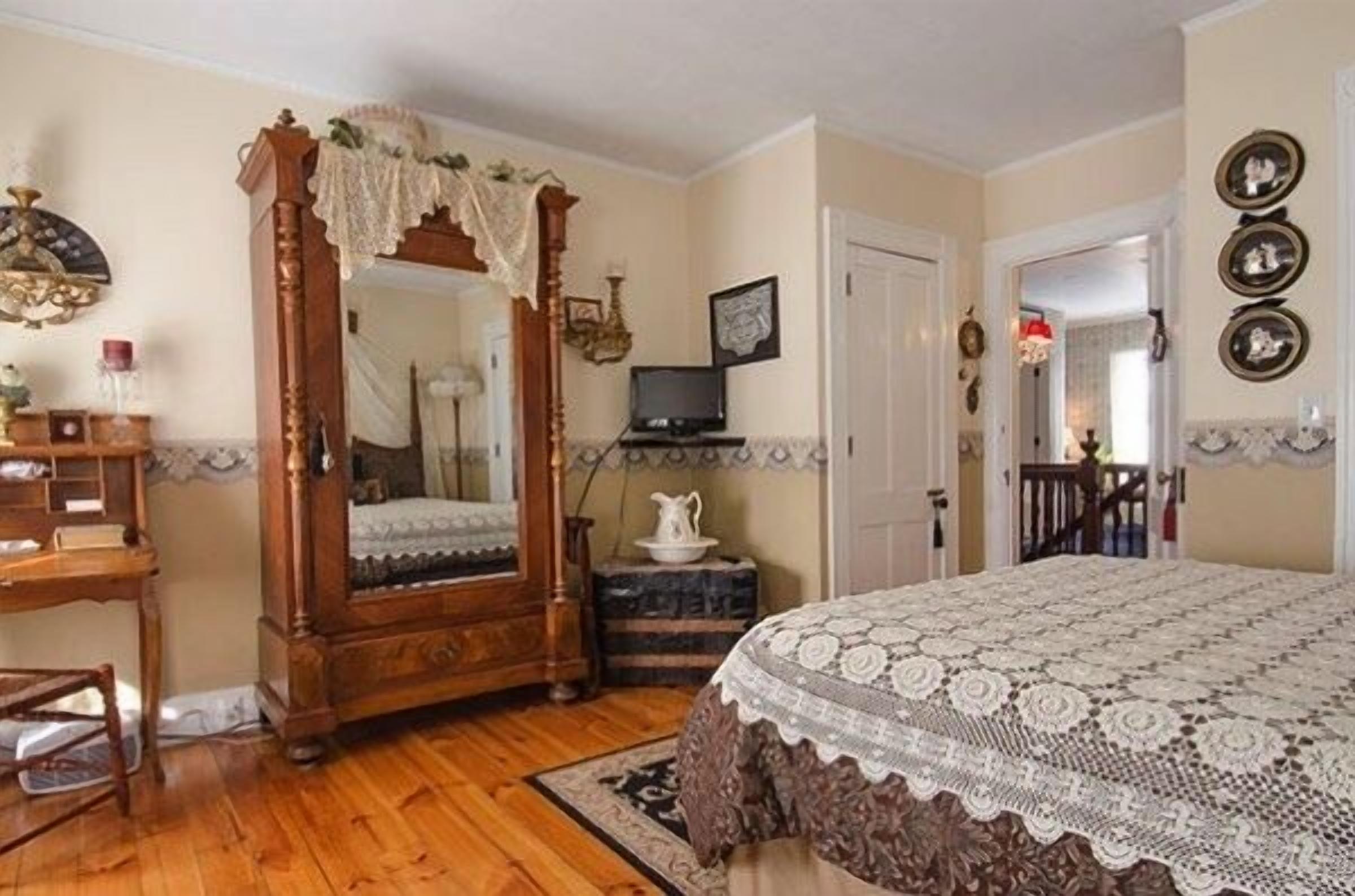 A bedroom with a wooden four-poster bed, a television, a small table with a pitcher, and a mirror.