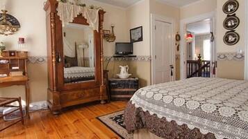 A bedroom with a wooden four-poster bed, a television, a small table with a pitcher, and a mirror.