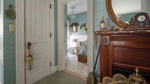 A hallway with a white door, a mirror with a clock, and a fireplace with decorative items. - The Tea Rose Inn at Plymouth (Plymouth)