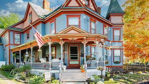 A large, two-story house with a prominent front porch, a chimney, and a flag. - The Tea Rose Inn at Plymouth (Plymouth)