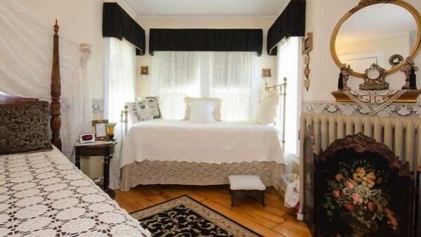 A bedroom with a large bed, a nightstand, a dresser, a mirror, and a fireplace. - The Tea Rose Inn at Plymouth (Plymouth)