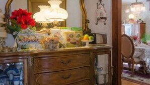 A wooden dresser with a mirror, a vase with red flowers, and various items on top. - The Tea Rose Inn at Plymouth (Plymouth)
