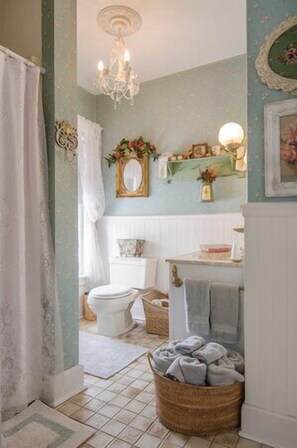 Bathroom features a vintage toilet, wicker basket, and chandelier.