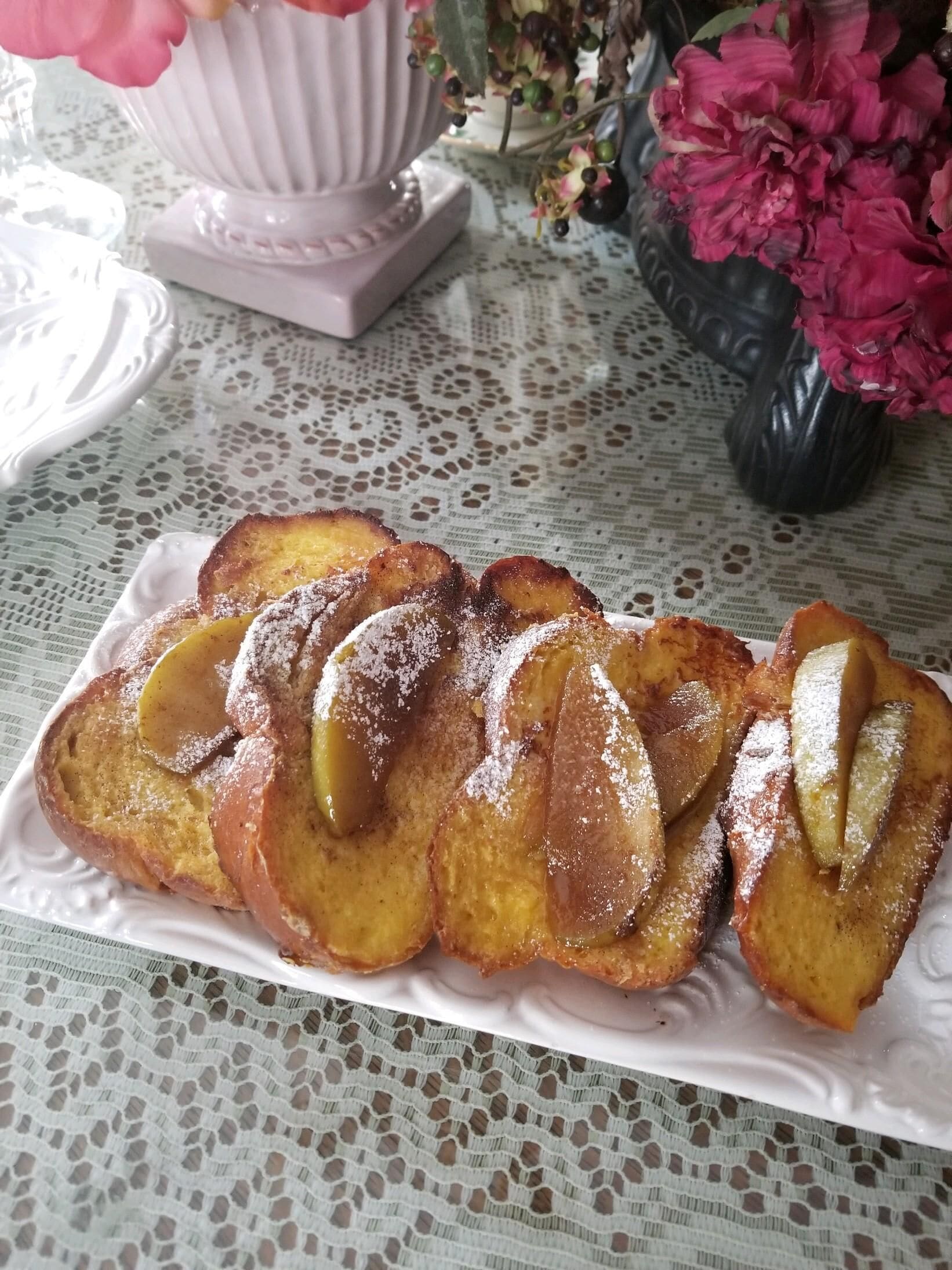 Una rebanada de pan con rodajas de manzana y azúcar glas sobre un plato blanco.