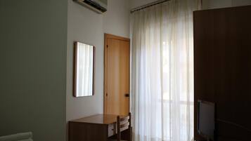 A room with a wooden desk, a television, and a window with sheer curtains.