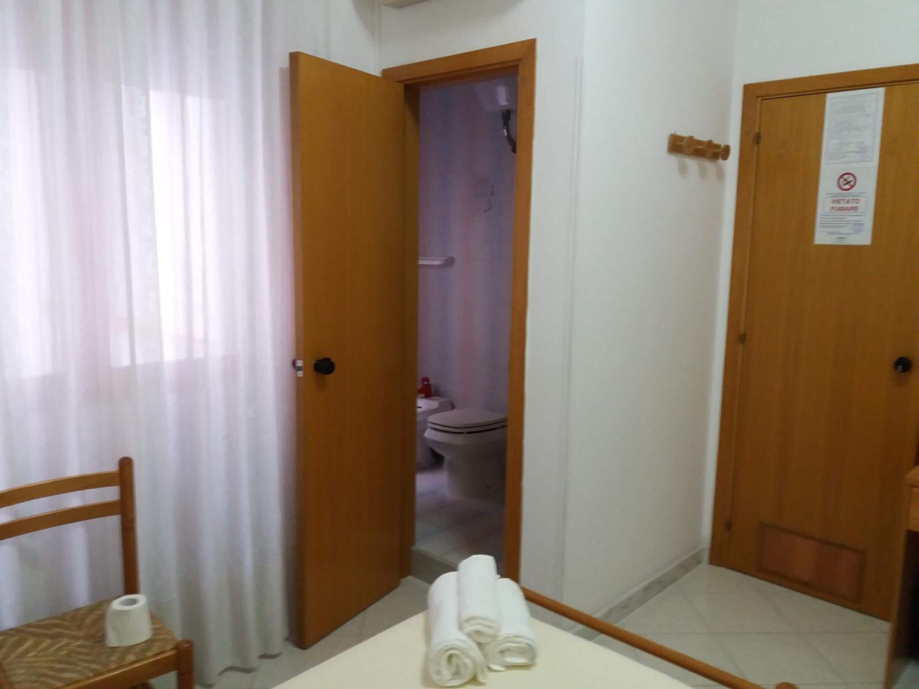 Un baño de hotel con puerta de madera, un inodoro visible desde la entrada y una toalla en el suelo.