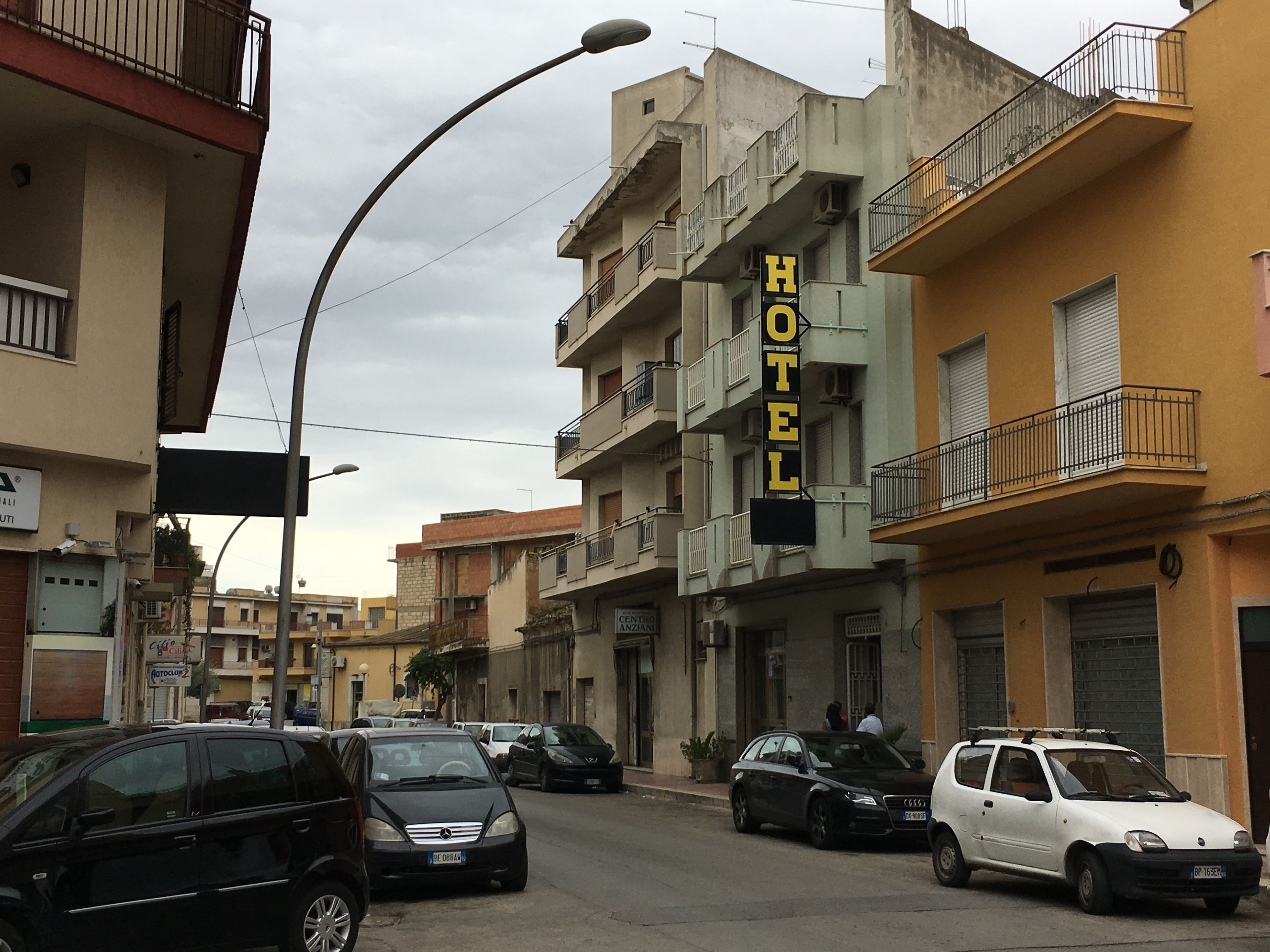 Un hotel con un letrero que dice "HOTEL" en letras grandes, varios balcones y coches estacionados en la calle.
