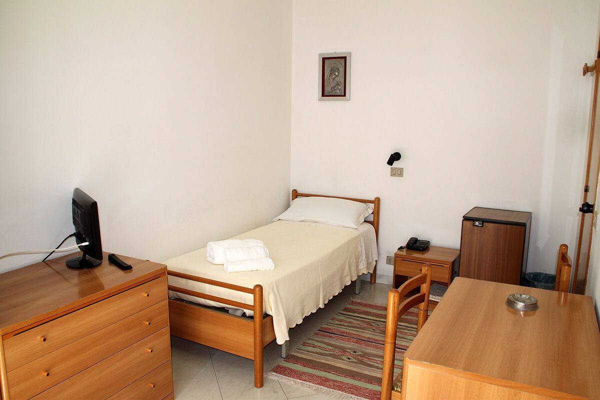 Une chambre à coucher comprenant un lit, un bureau, une chaise, une commode, une table de chevet, une lampe et un petit placard.
