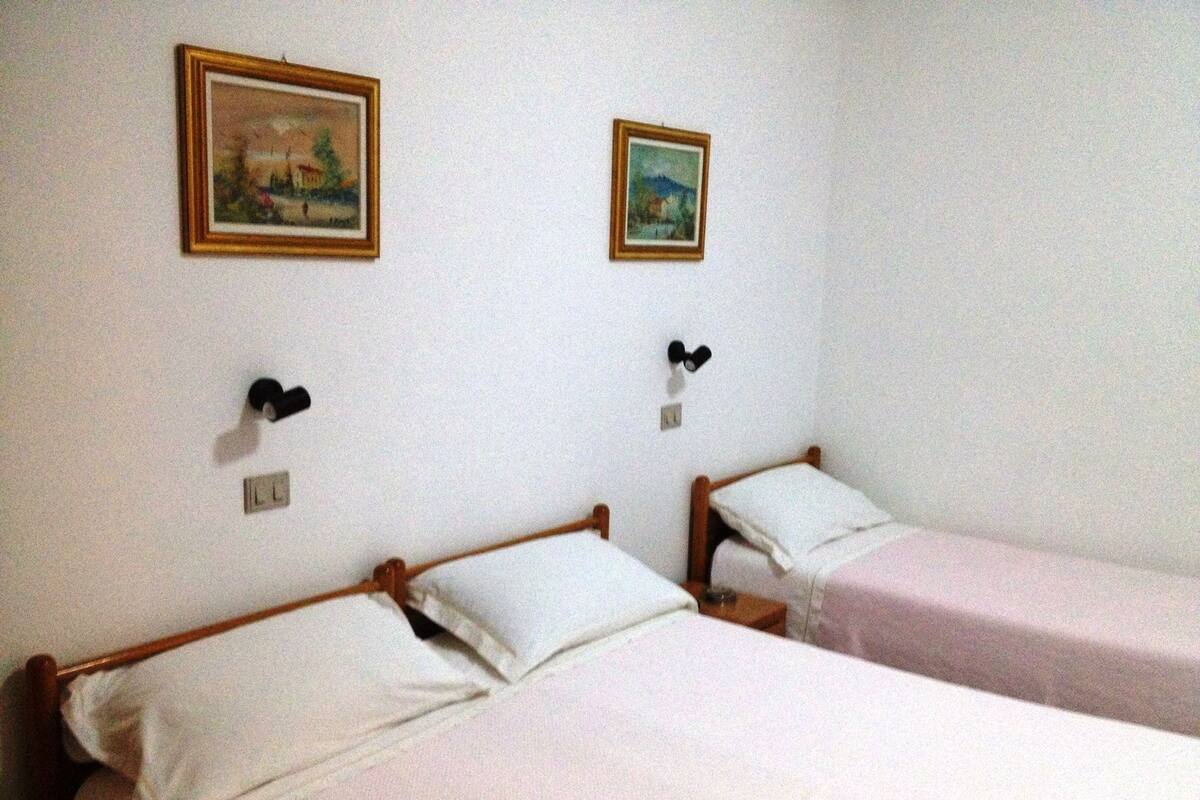 Deux lits simples avec des cadres en bois et une literie blanche, un petit radiateur fixé au mur et deux tableaux encadrés accrochés au mur.