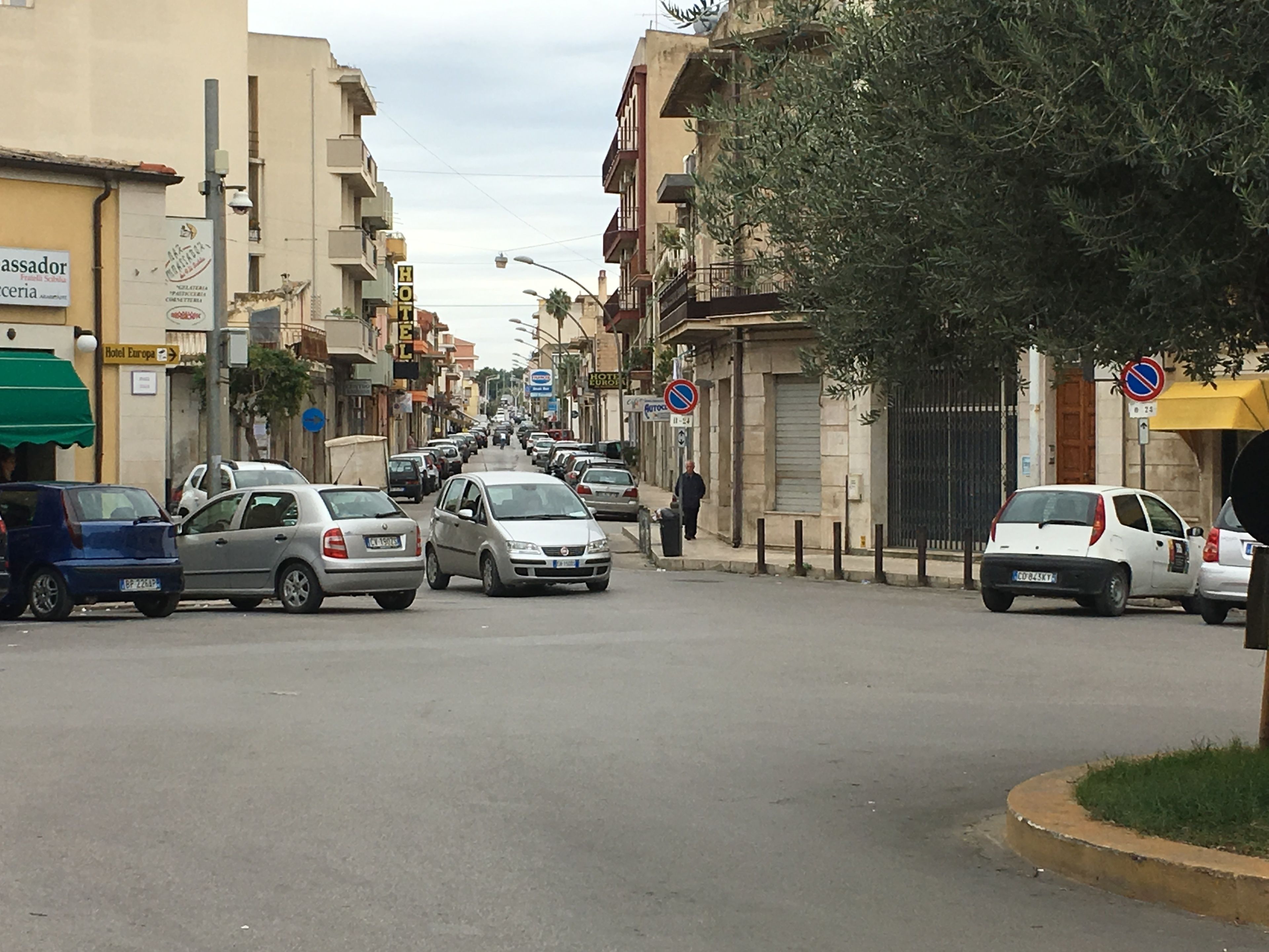 A street with parked cars, buildings, and a pedestrian.