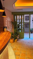 Un área de recepción con mostrador de madera, plantas en macetas y una puerta verde que da al exterior.