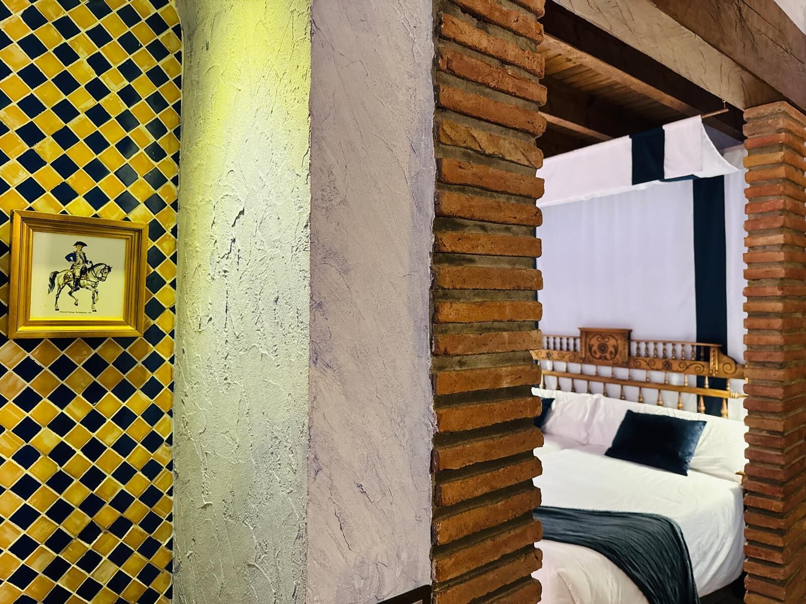 A room with a bed, a framed picture on the wall, and a brick pillar.