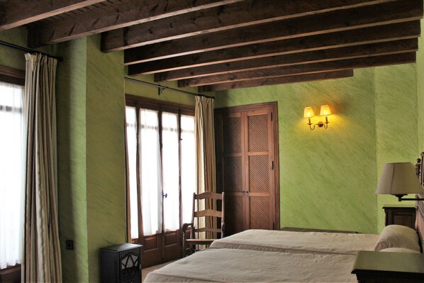 A room with a bed, a chair, a wooden door, and a wall-mounted lamp.