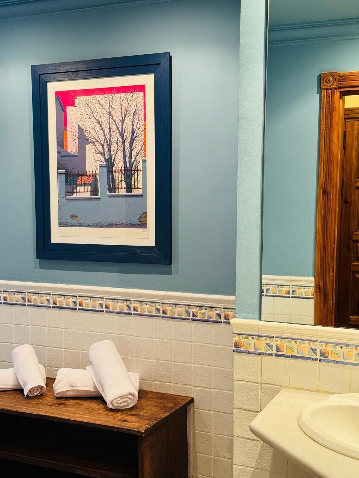 A bathroom with a framed picture, a wooden bench with towels, and a sink.