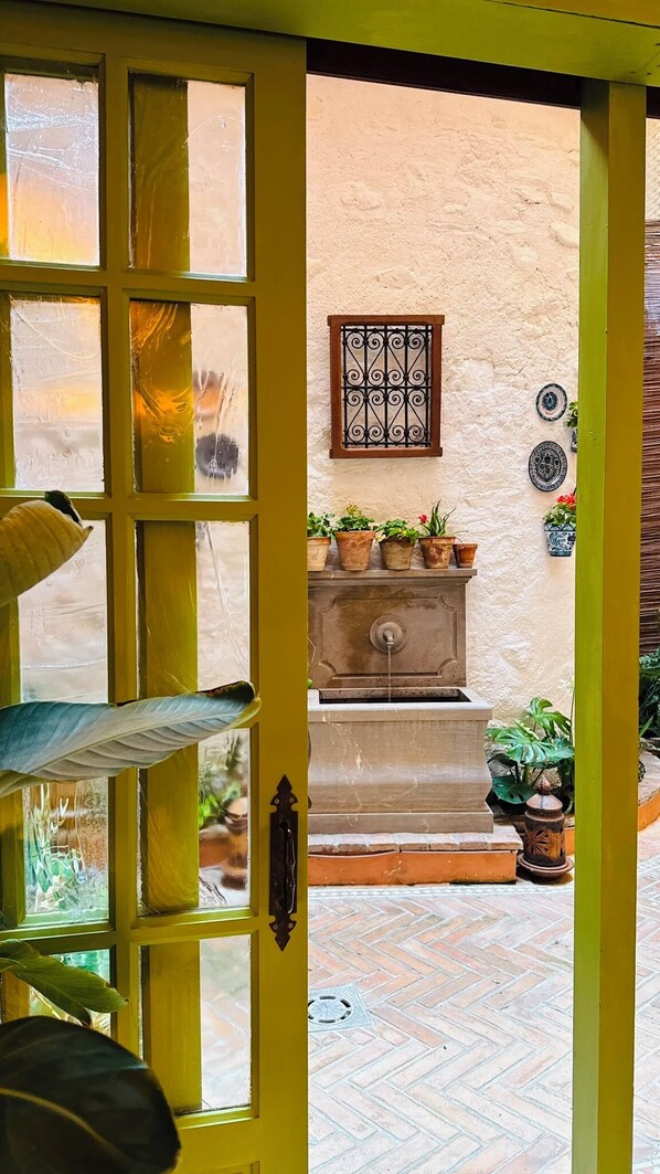 A yellow door with a window, a stone wall, a metal gate, and potted plants.