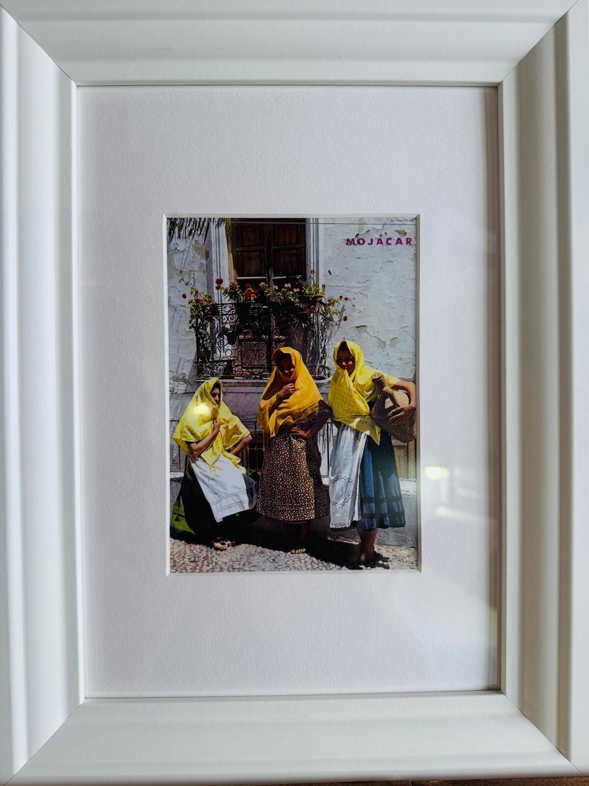 Een ingelijste foto van drie vrouwen in traditionele kleding, met een gebouw en een bord waarop 'MOJACAR' staat.