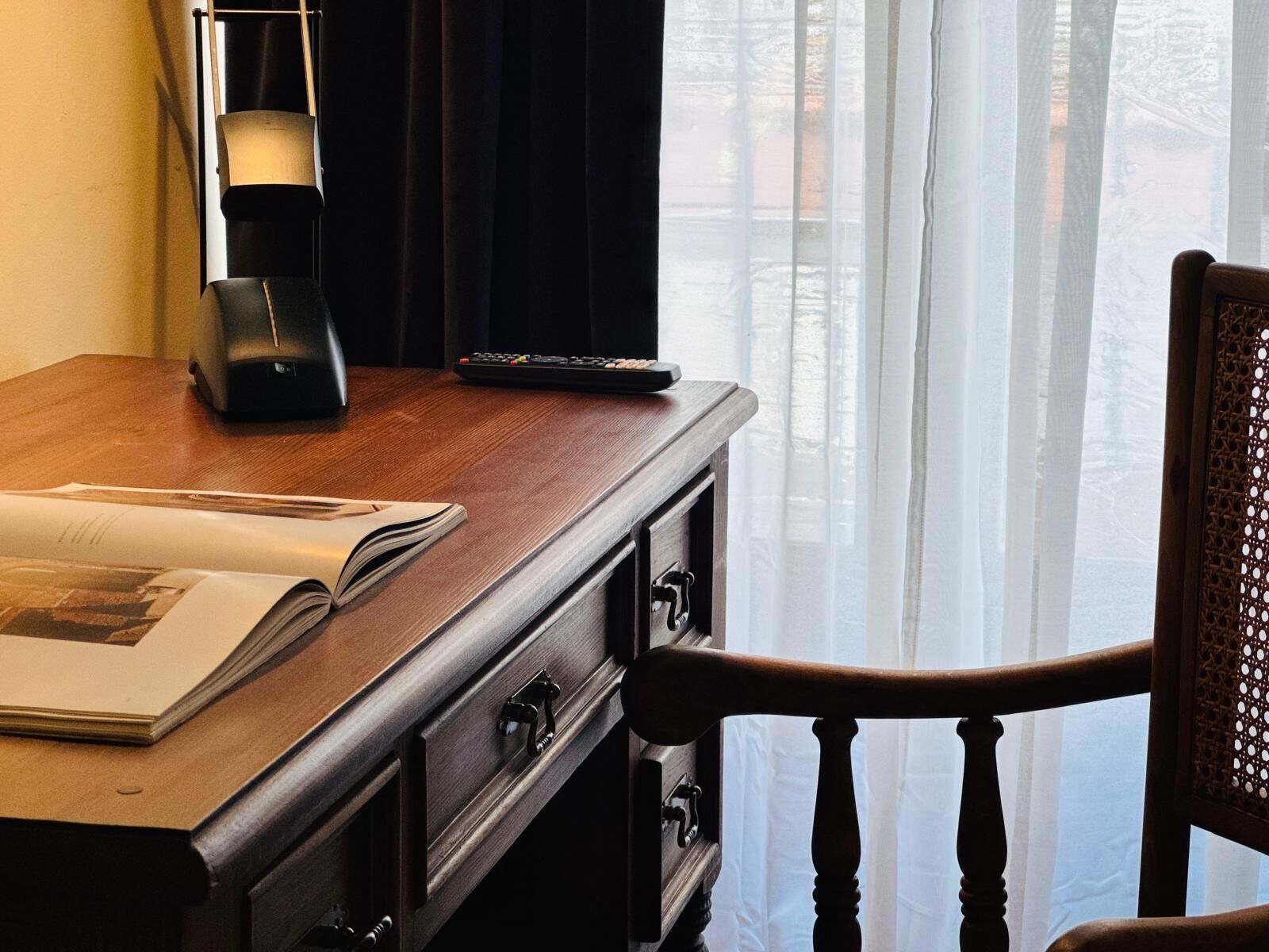 A wooden desk with a lamp, remote control, and an open book.