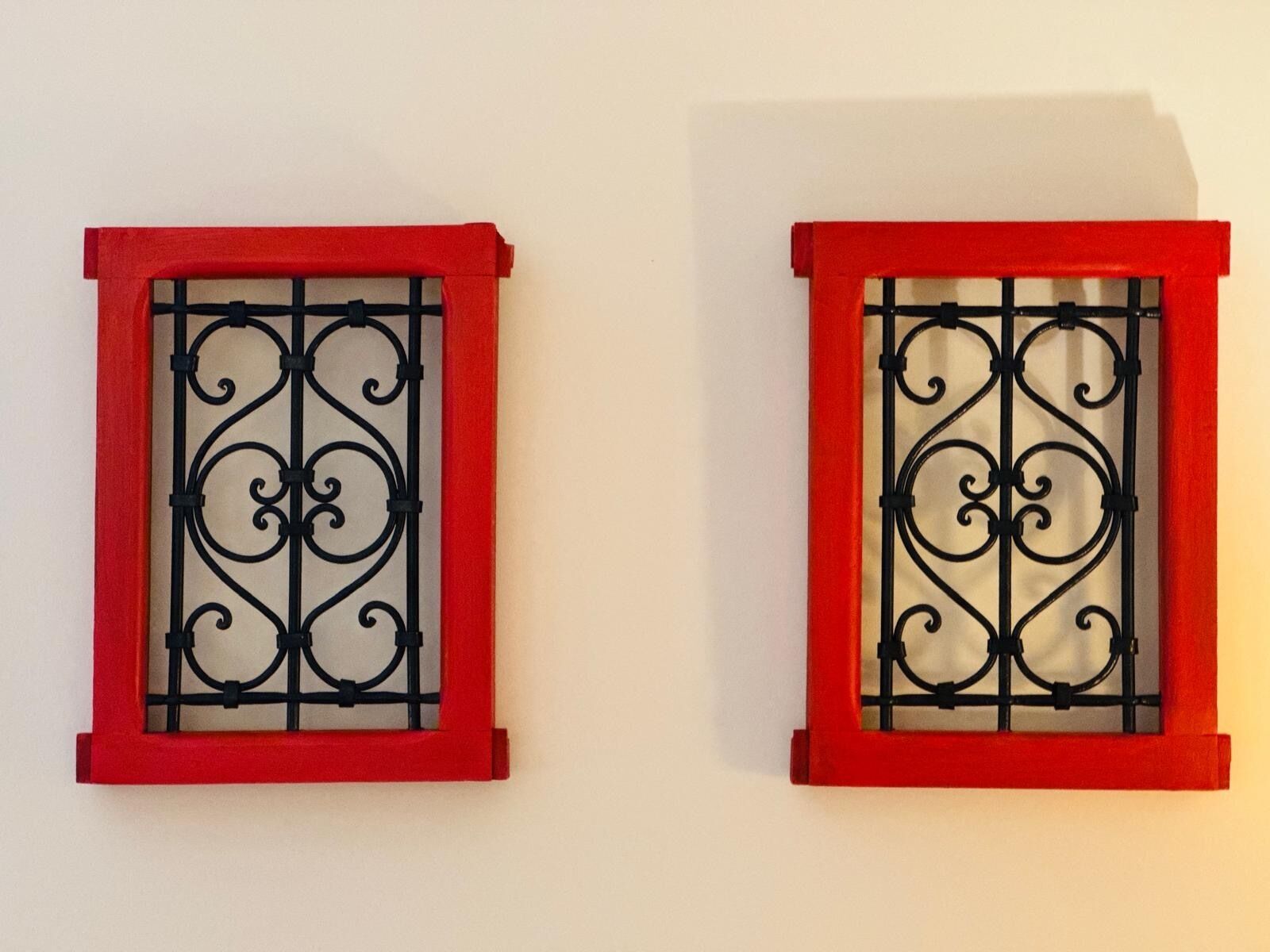 Dos ventanas con marcos rojos y detalles de hierro forjado negro.