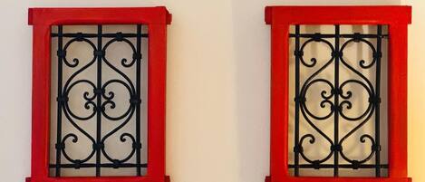 Dos ventanas con marcos rojos y detalles de hierro forjado negro.