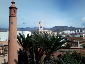 A tall tower with a cross at the top, a building with a bell tower, and mountains in the background. - Hotel Boutique Palacete del Corregidor (Almunecar)