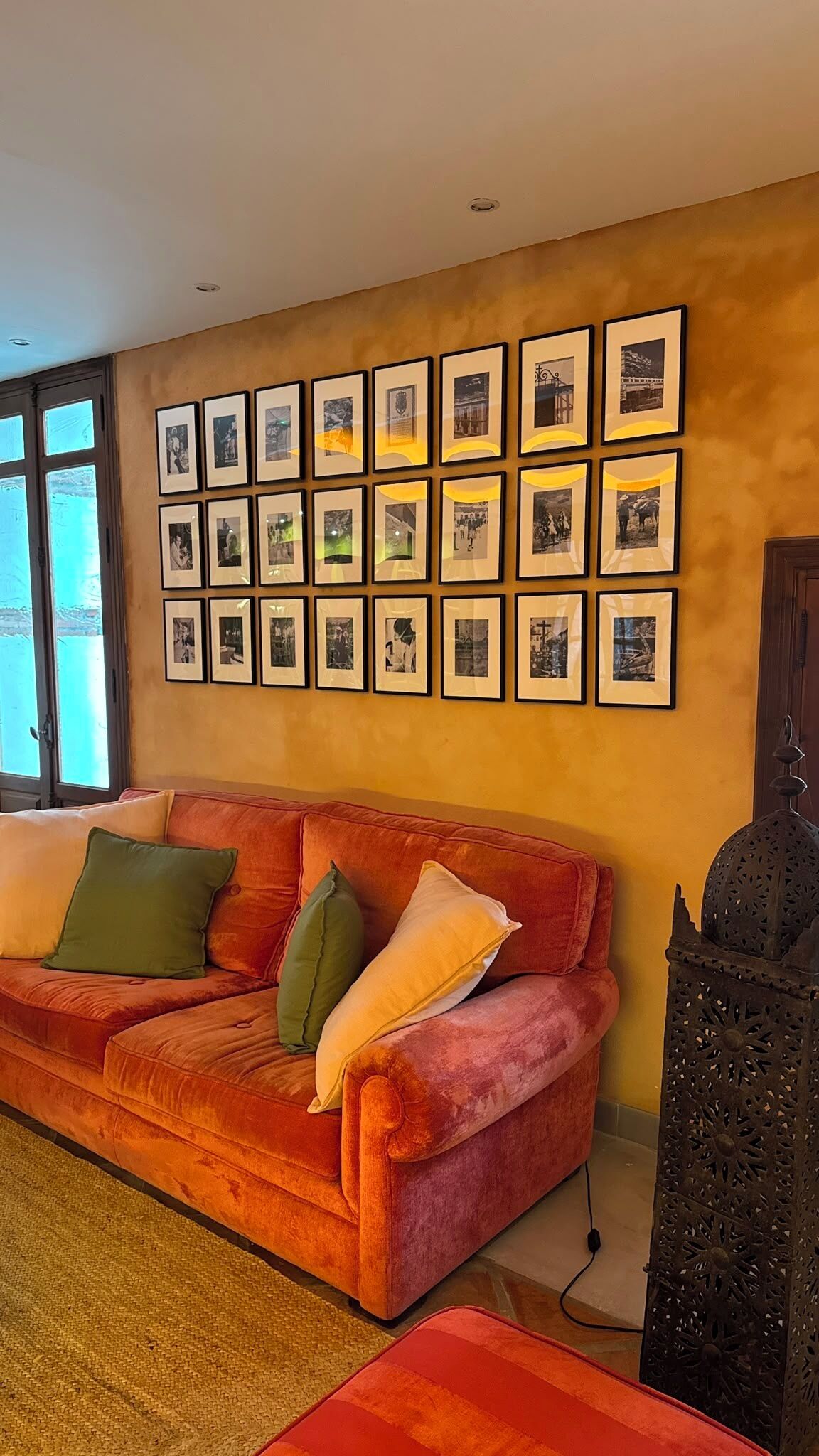 Una sala de estar con un sofá rojo, varias fotografías enmarcadas en la pared y una pieza decorativa de metal a la derecha.
