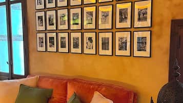 Una sala de estar con un sofá rojo, varias fotografías enmarcadas en la pared y una pieza decorativa de metal a la derecha.