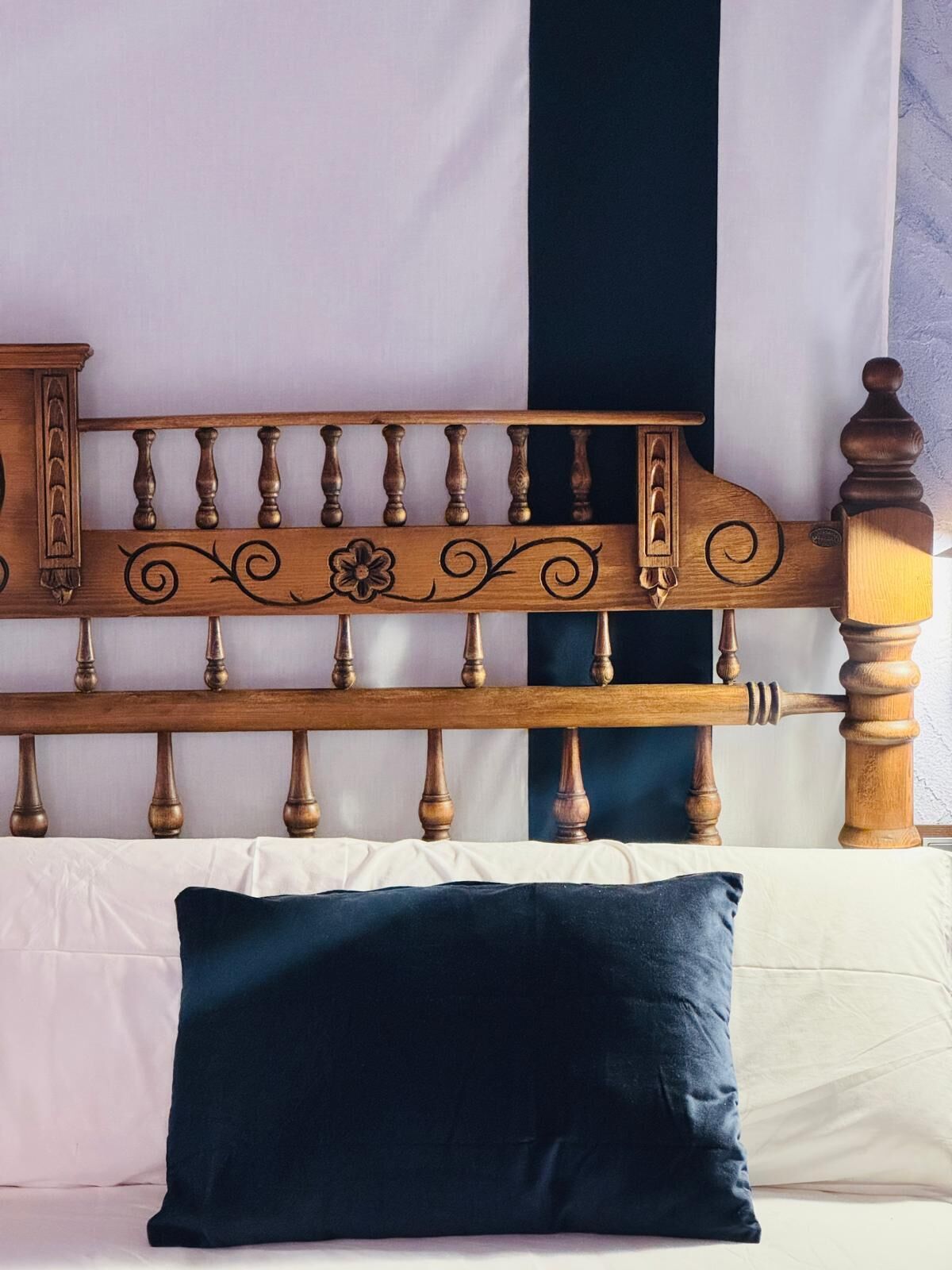 A bed with a wooden headboard, a dark blue pillow, and white bedding.