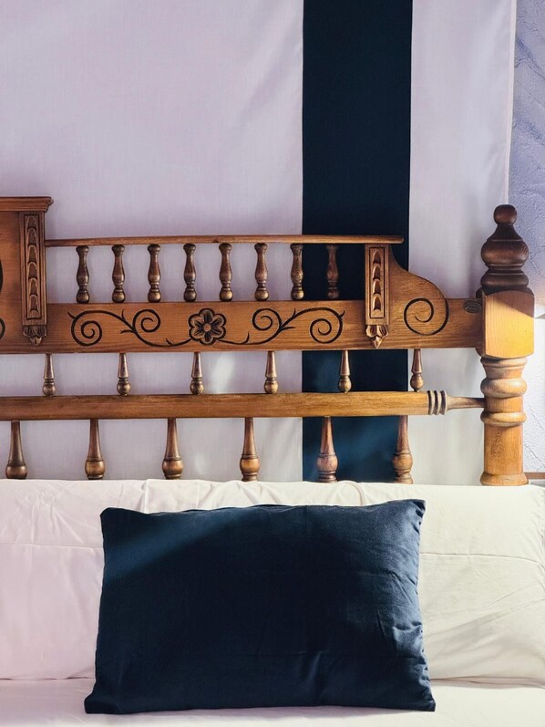 Una cama con cabecera de madera, almohada azul oscuro y ropa de cama blanca.