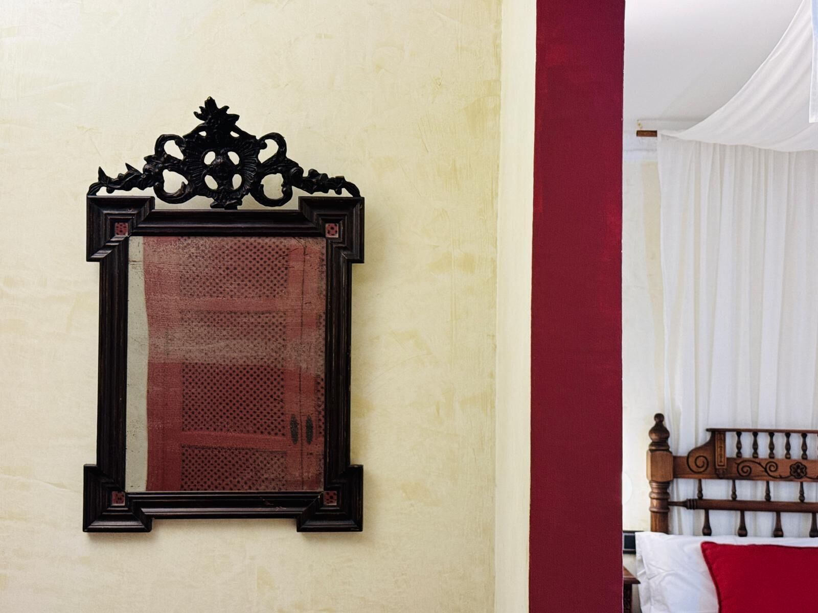 A room with a bed, a wall-mounted mirror, and a red accent wall.