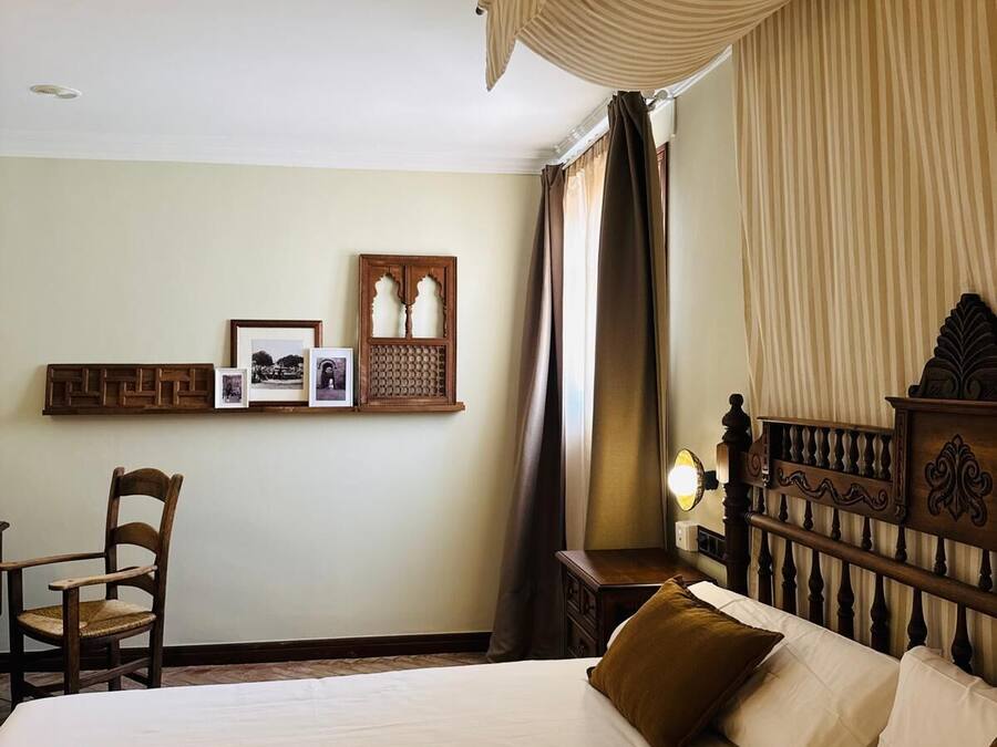 Habitación de hotel con una cama grande, una silla, cabecero de madera y un cuadro colgado en la pared.
