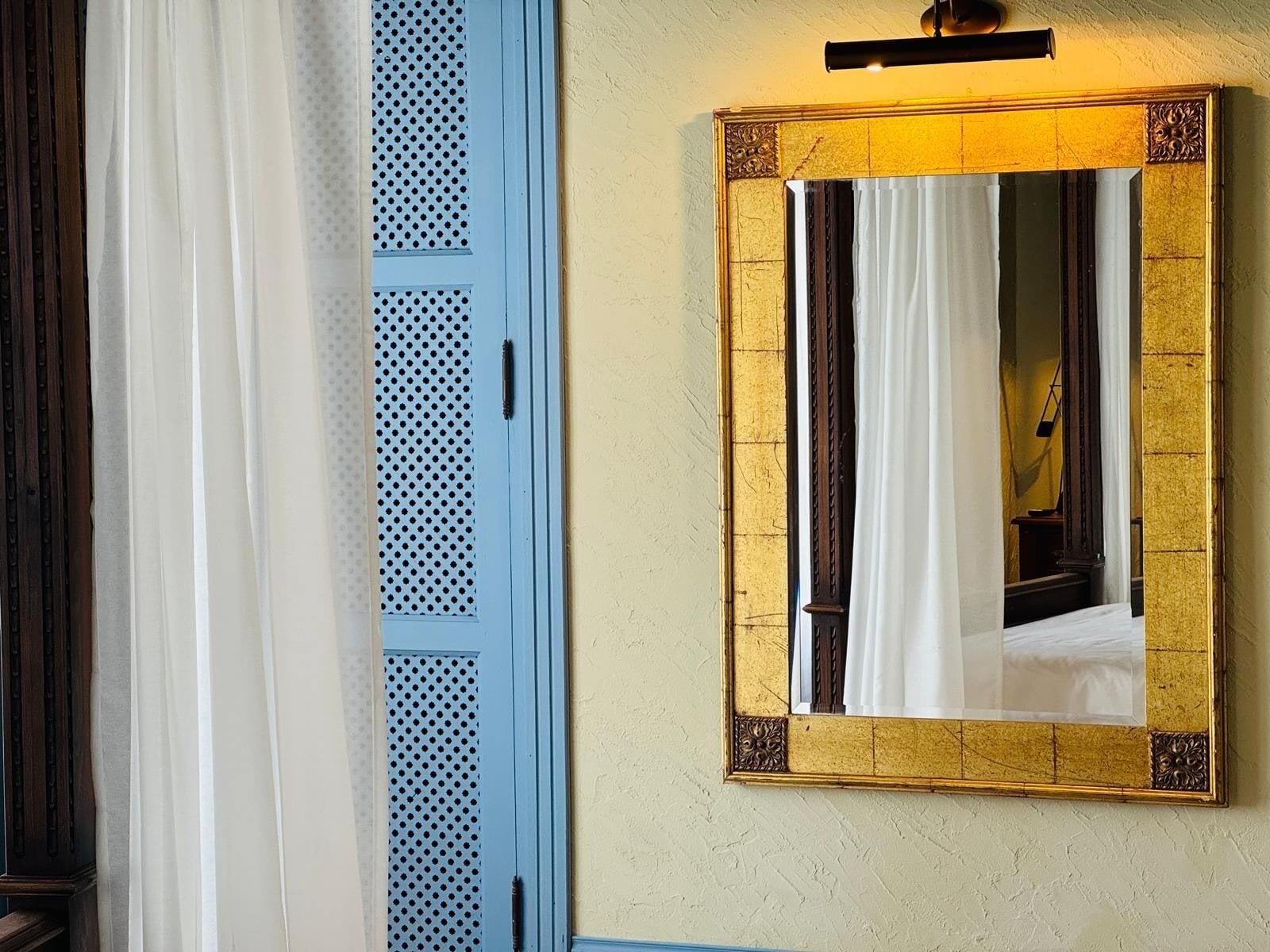 A room with a blue door, a gold-framed mirror, and a light fixture above it.