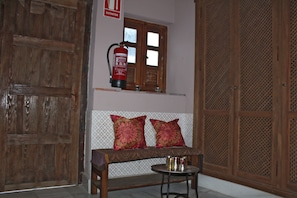 A room with a wooden door, a fire extinguisher mounted on the wall, a bench with cushions, and a small table.