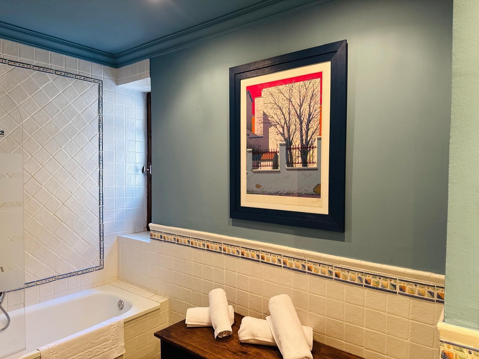 A bathroom with a bathtub, a framed picture on the wall, and a tiled backsplash.