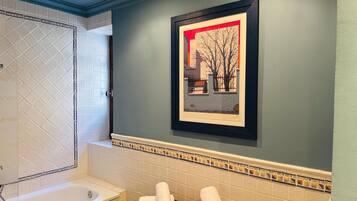 A bathroom with a bathtub, a framed picture on the wall, and a tiled backsplash.
