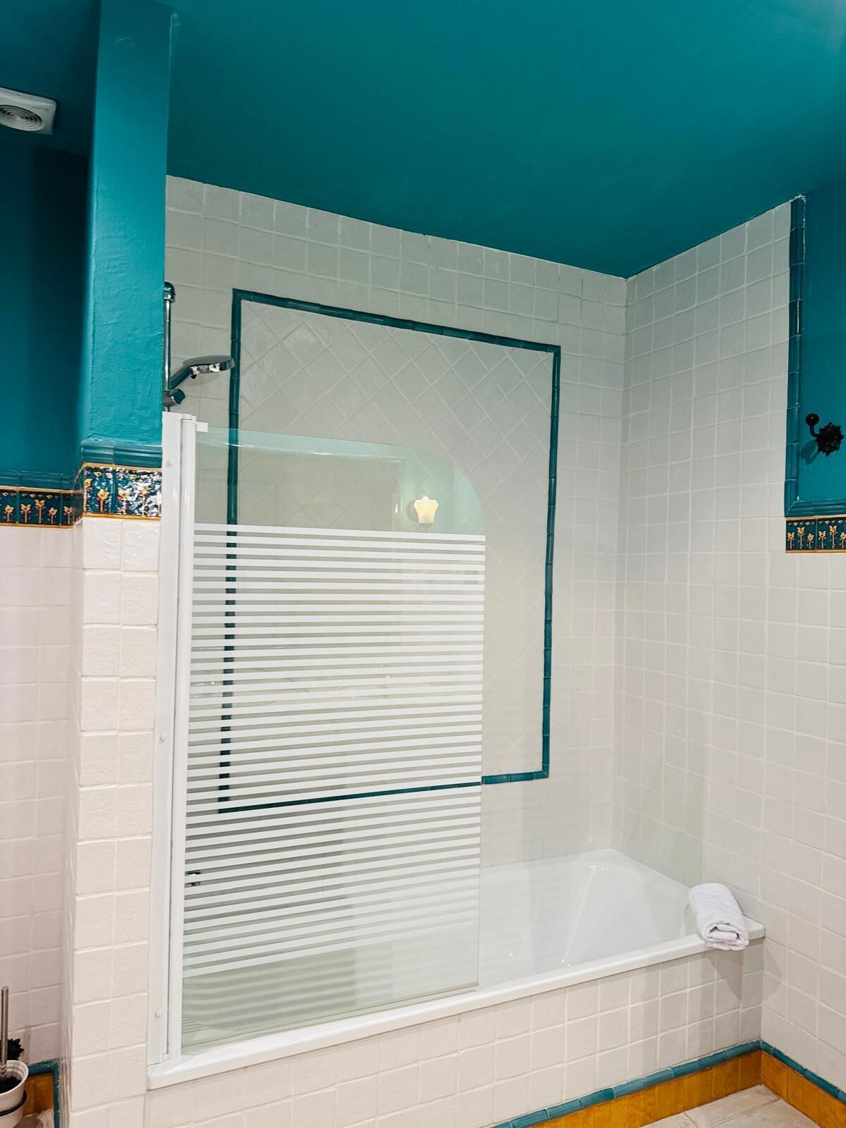 Ein Badezimmer mit einer gläsernen Duschkabine, einer weißen Badewanne und einer weiß gefliesten Wand mit türkisfarbenen Akzenten.