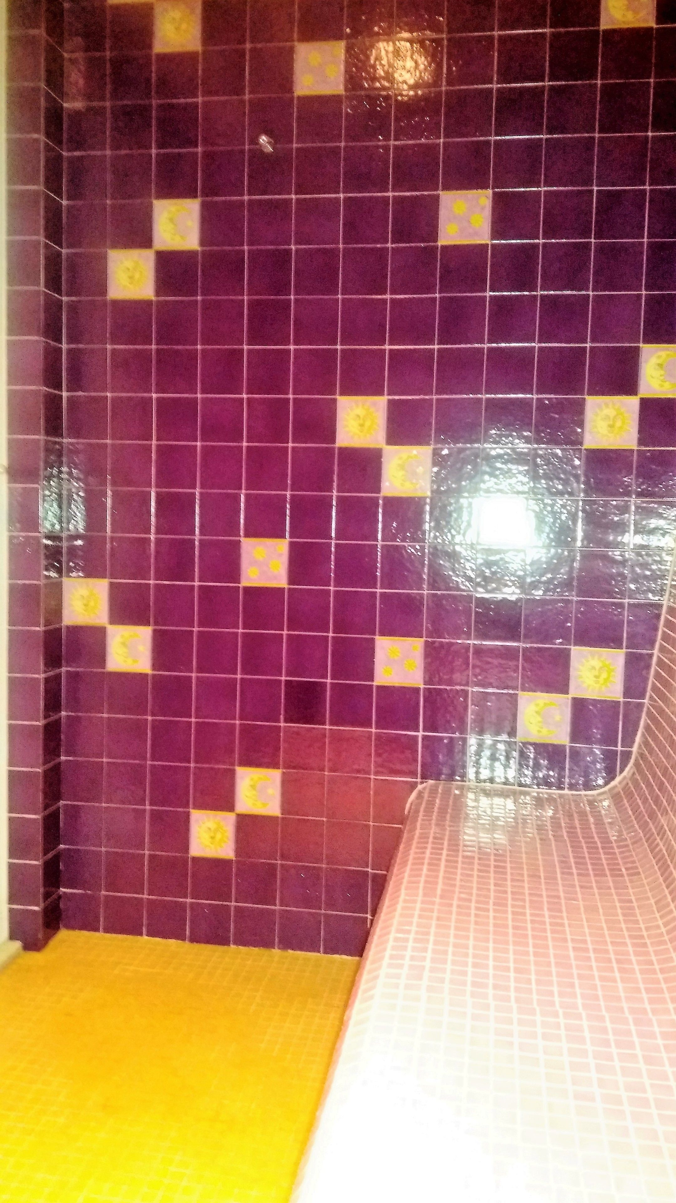 A tiled wall with purple tiles and yellow accents, a yellow floor, and a curved white structure.
