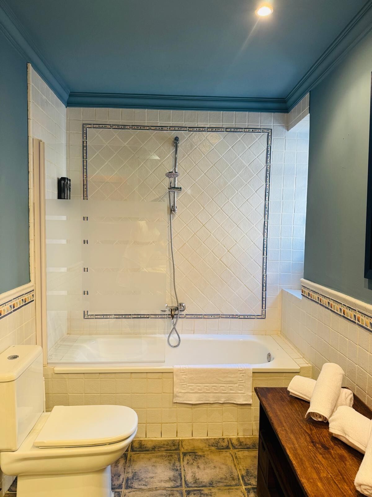 A bathroom with a bathtub, toilet, and a wooden vanity with towels.