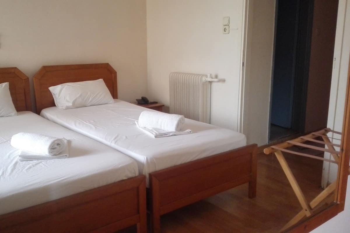Two single beds with wooden frames and white linens, a wooden nightstand with a phone, and a radiator on the wall.