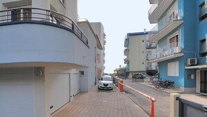 Eine schmale Stadtstraße mit Wohnhäusern, einem weißen Auto, das am Straßenrand geparkt ist, und einem Fahrradständer.