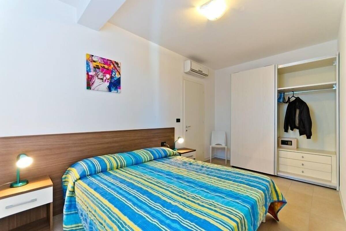 Une chambre à coucher comprenant un lit, une table de chevet, une lampe, un appareil de climatisation et un placard avec des vêtements suspendus.