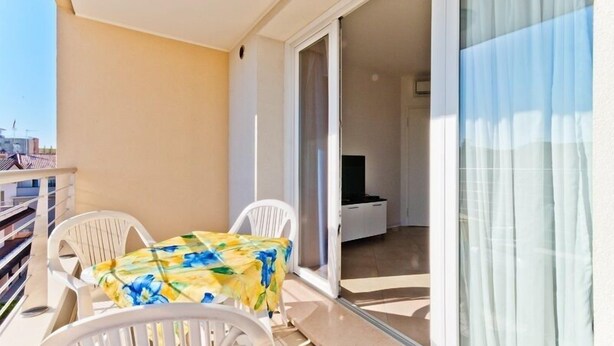 Ein Balkon mit Tisch und Stühlen, eine Schiebetür zu einem Zimmer und Blick auf die Stadt.