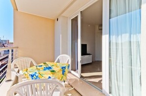 Un balcón con mesa y sillas, un ventanal corredero que da a una habitación y vistas a la ciudad.