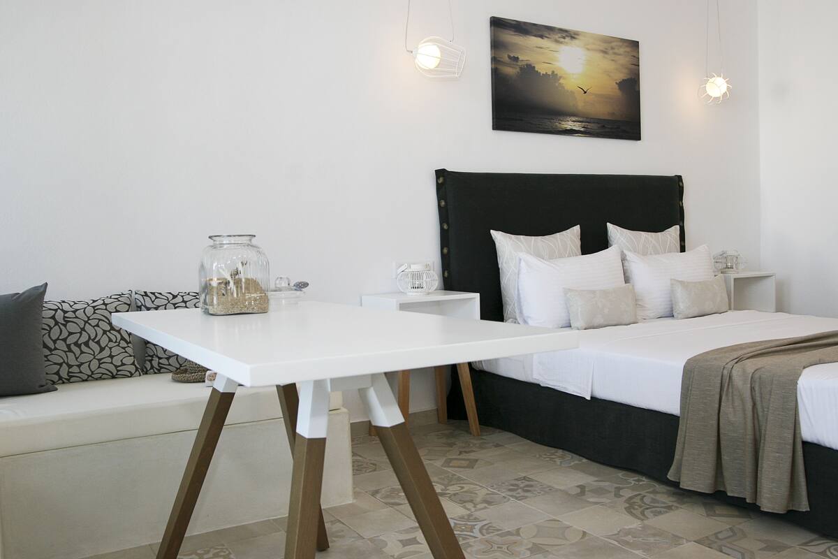 Een slaapkamer met een bed, nachtkastje, witte tafel, bank en een aan de muur hangend schilderij.
