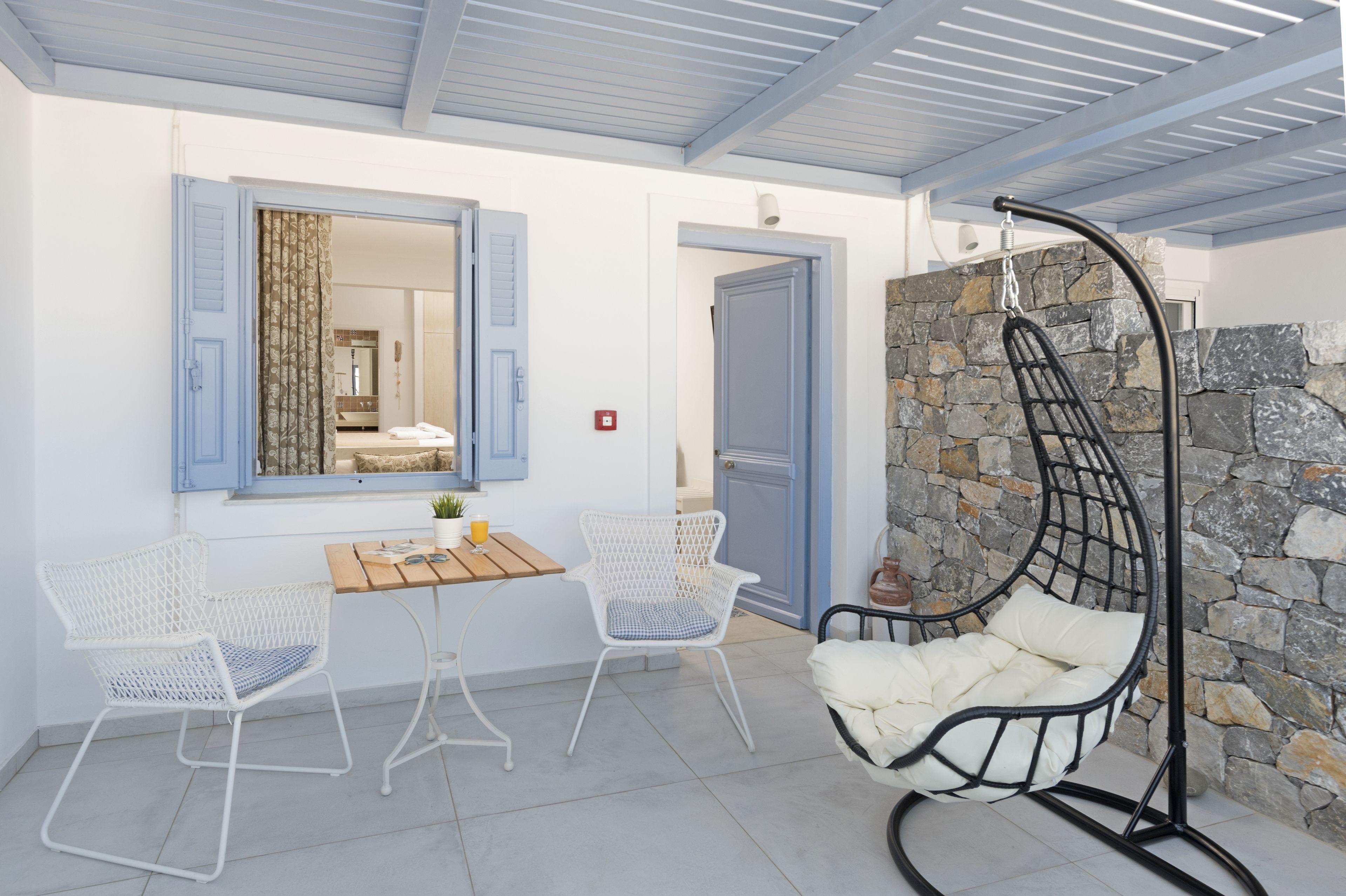 A room with a stone wall, a hanging chair, and two white chairs with a table.