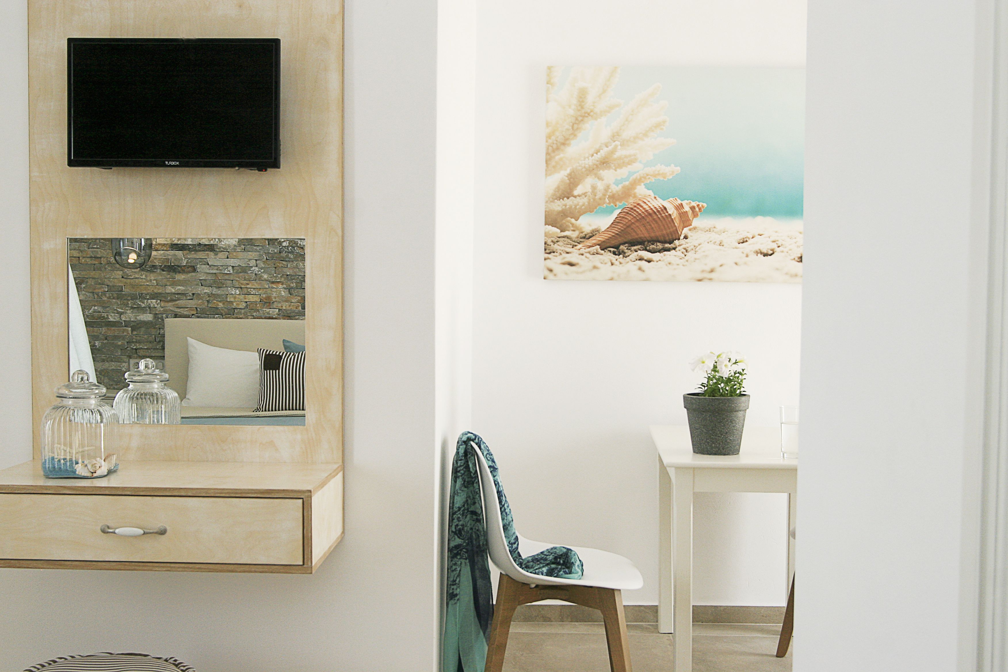 A room with a TV mounted on a wooden wall, a stone backsplash, a mirror, a chair with a blue cushion, and a painting of a beach scene.