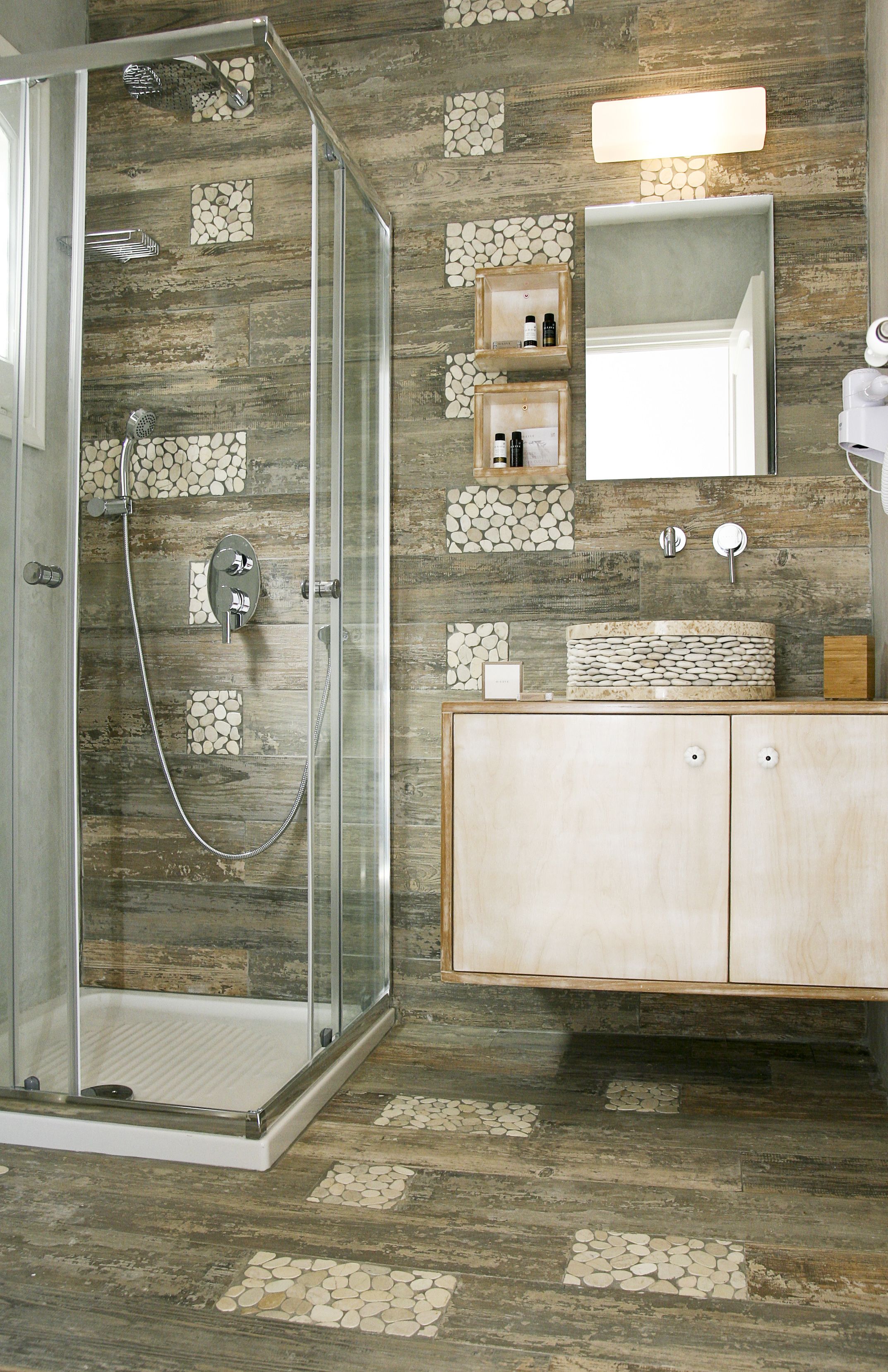 Un baño con cabina de ducha de vidrio, tocador de madera con lavamanos y espejo.