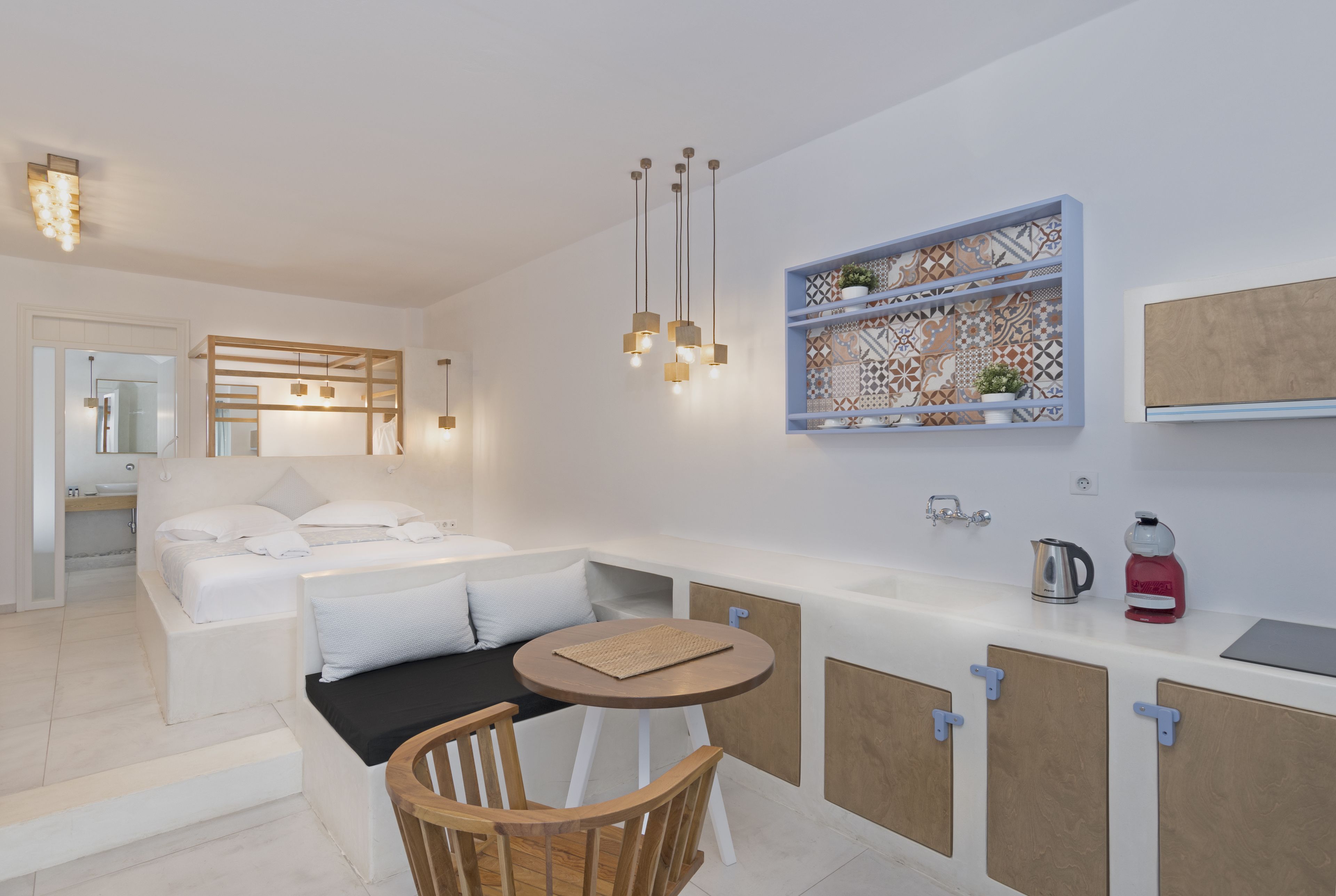 Una habitación de hotel moderna con cama, una pequeña mesa de comedor, una silla, un lavamanos y un estante decorativo.